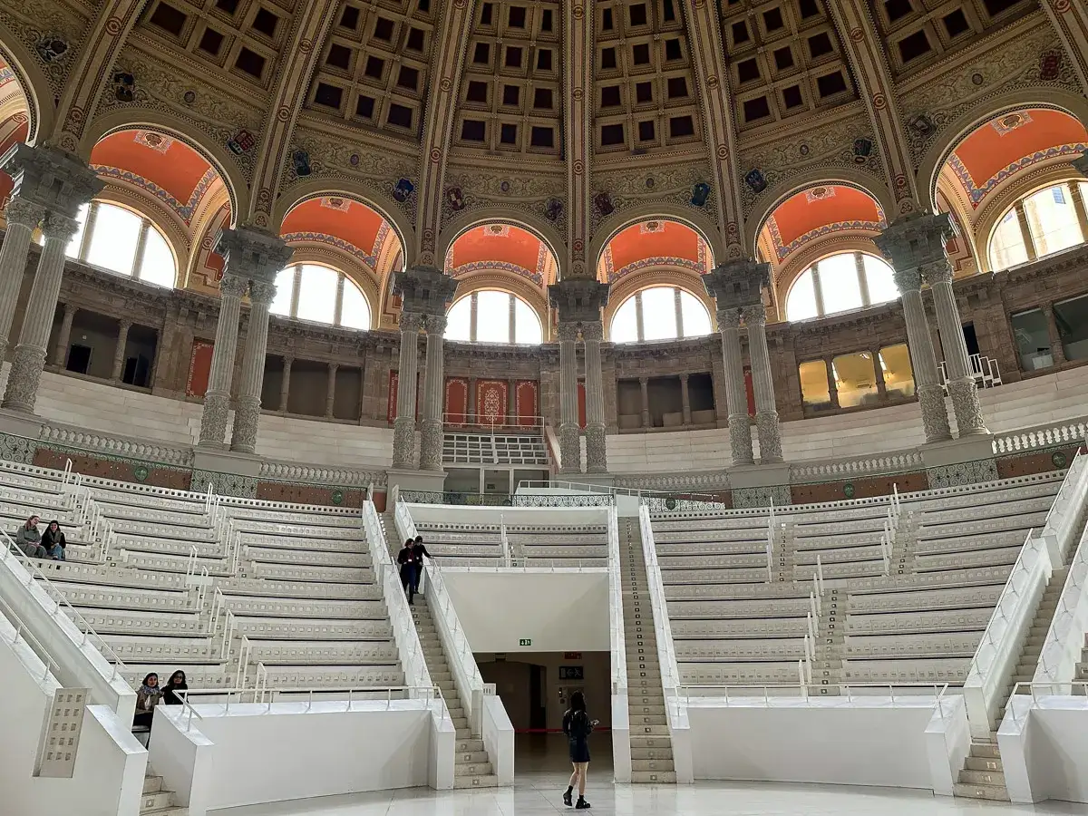 Wnętrze muzeum sztuki w Barcelonie z amfiteatralnymi schodami i ozdobną kopułą.