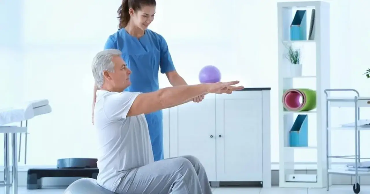 Fizjoterapia ambulatoryjna: mężczyzna ćwiczy z fizjoterapeutką, która go wspiera. W tle sprzęt rehabilitacyjny.