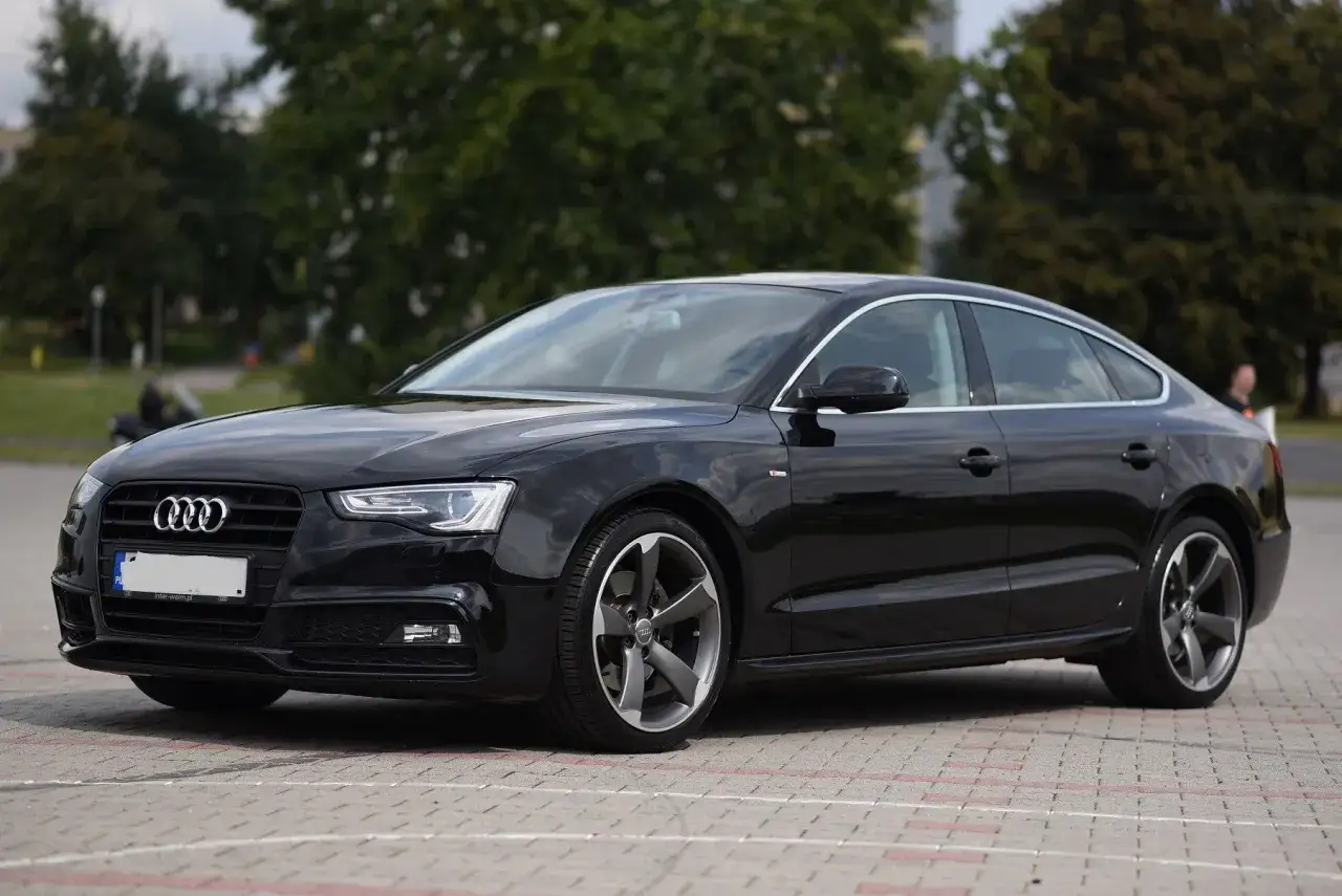 Elegancka, czarna Audi A5 Sportback na parkingu. Ta fotografia samochodowa ukazuje sportowy charakter auta.