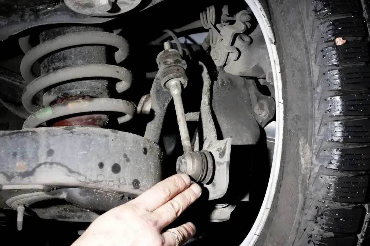 Dłoń wskazuje na zużyty łącznik stabilizatora, jeden z objawów awarii gumy stabilizatora.