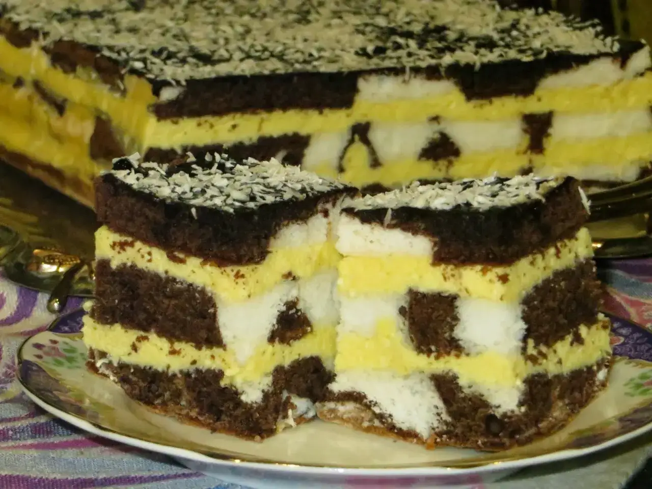 Pyszne ciasto z serem, przełożone kremem i biszkoptem, posypane wiórkami kokosowymi.