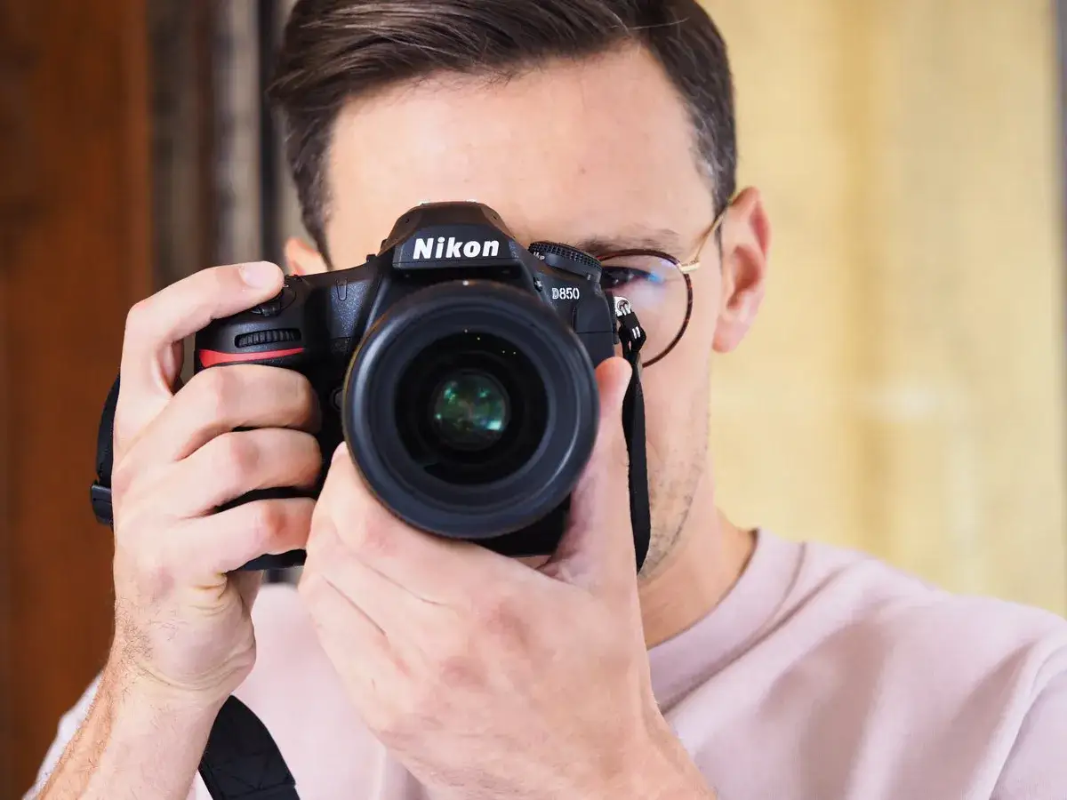 Mężczyzna z okularami trzyma aparat Nikon D850, gotowy do testu.