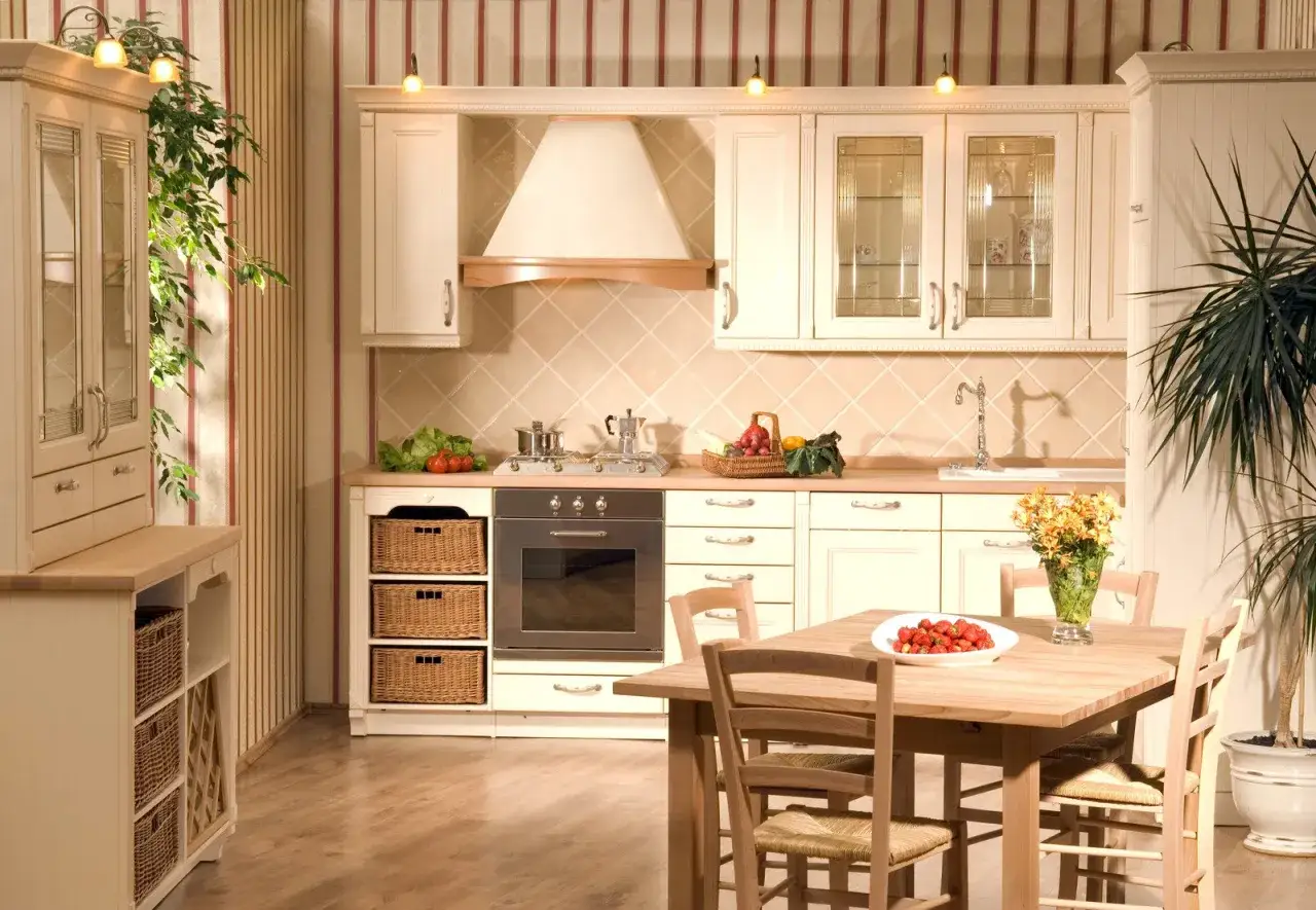 Przytulne wnętrze kuchni w stylu wiejskim. Jasne meble, wiklinowe kosze i drewniany stół tworzą ciepłą atmosferę.