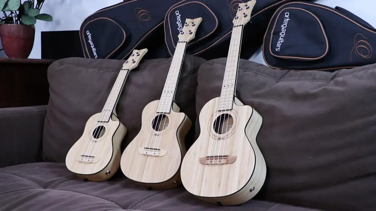 Trzy drewniane ukulele leżą na brązowej kanapie. To małe, czterostrunowe instrumenty, idealne do nauki gry.