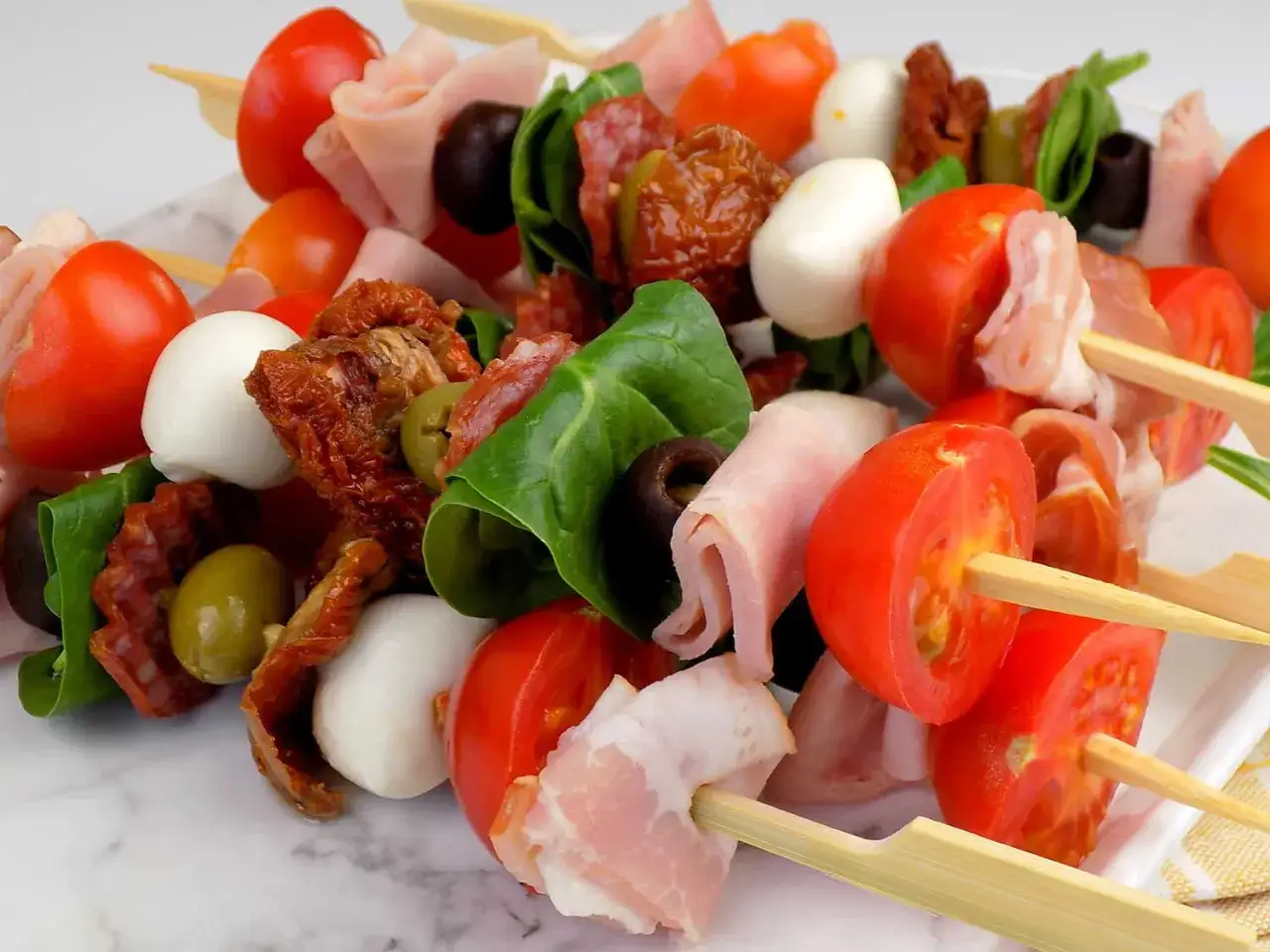 Kolorowe szaszłyki z pomidorkami, mozzarellą, wędlinami i oliwkami – idealne zimne przekąski na grilla.