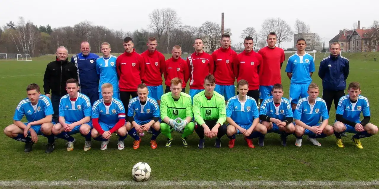 Drużyna Piasta Gliwice zawodnicy w niebieskich i czerwonych strojach pozują do zdjęcia na boisku.