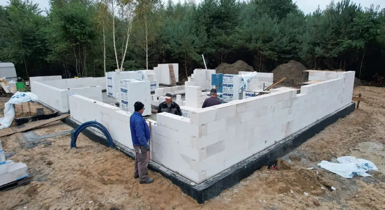 Kiedy hydraulik na budowie, pracownicy układają białe pustaki, tworząc fundamenty domu.