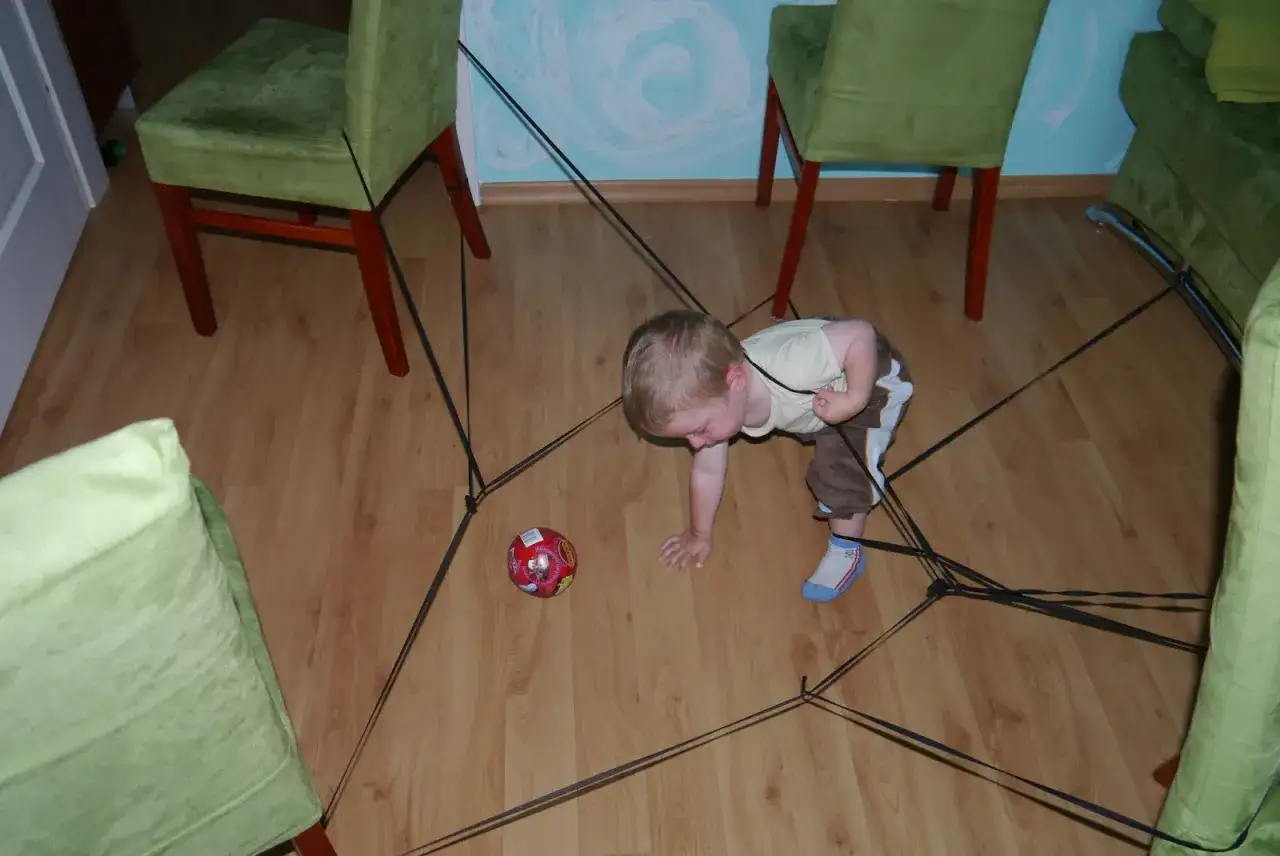 Dwulatek wplątany w czarne sznurki, obok piłka. Kreatywne zabawy z dwulatkiem w domu.