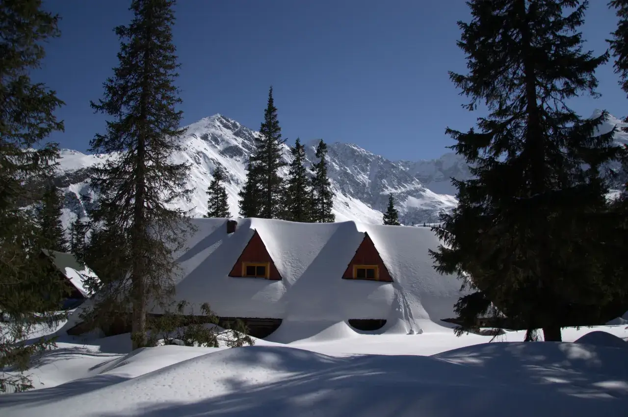 Zimowy krajobraz Tatr z zasypanym śniegiem schroniskiem. Idealne miejsce na wędr&oacute;wkę, jeśli zastanawiasz się, jaki szlak zimą w Tatrach wybrać.