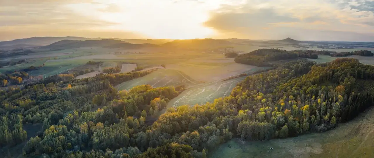Krajobraz przypomina krainę wygasłych wulkanów, z łagodnymi wzgórzami porośniętymi lasami i polami, skąpanymi w złotym świetle zachodzącego słońca.