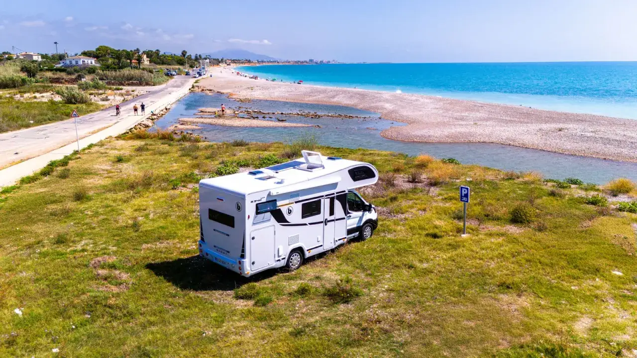 Kamper stoi na trawie przy plaży. Czy na kampera trzeba mieć prawo jazdy? To zależy od jego masy.