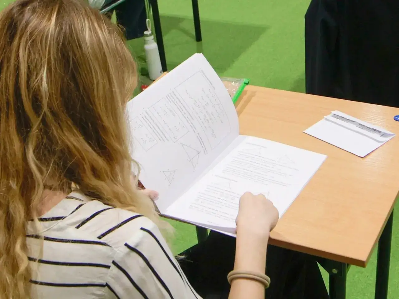 Dziewczyna z blond włosami pochyla się nad arkuszem z zadaniami matematycznymi, kiedy próbne matury. Skupiona na rozwiązywaniu problemów.