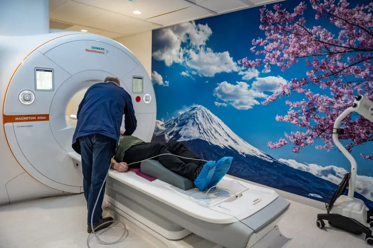 Pacjent leży na łóżku rezonansu magnetycznego. Personel przygotowuje badanie, by uniknąć powikłania po rezonansie magnetycznym bez kontrastu.