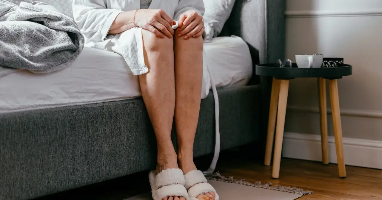 Kobieta w szlafroku siedzi na ł&oacute;żku, rozważając naturalne zioła na nietrzymanie moczu.