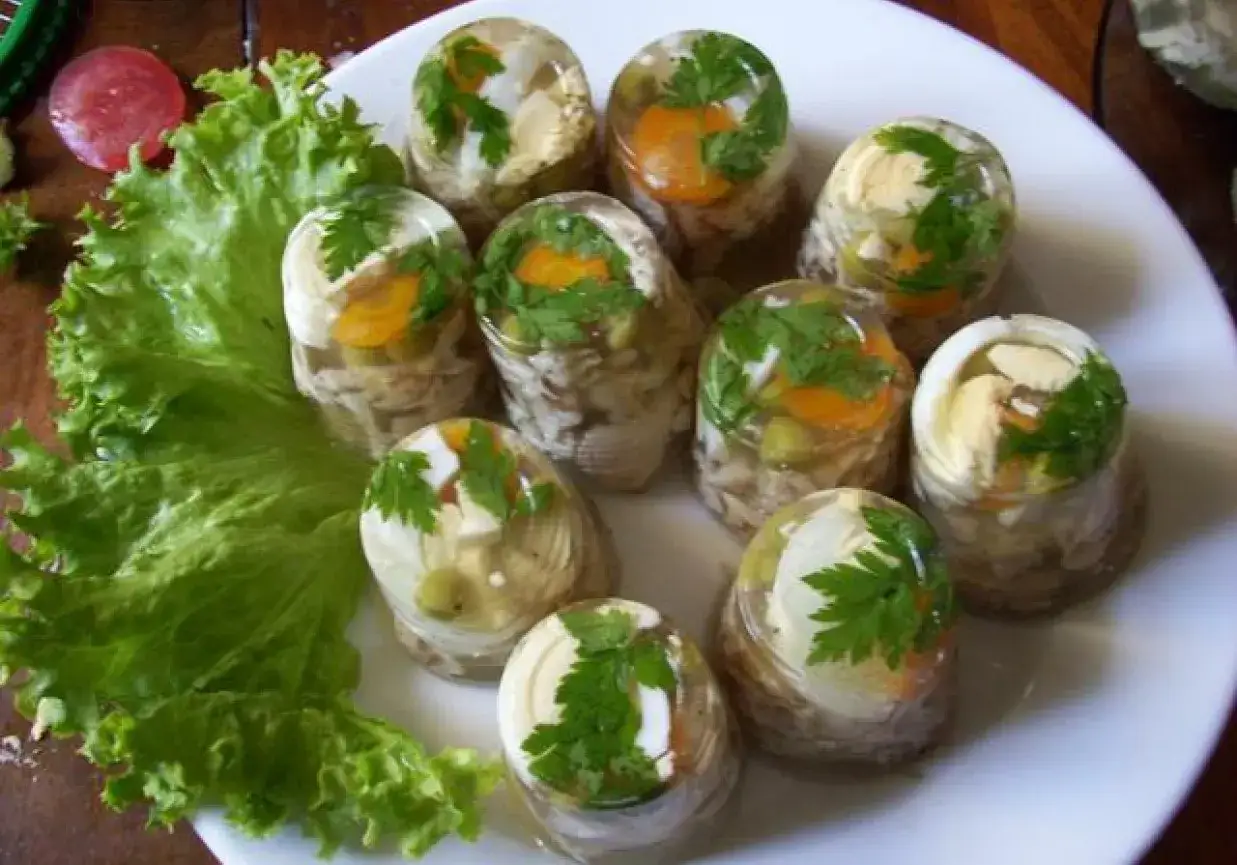 Porcja galaretek z kurczaka z marchewką i pietruszką, podana na liściu sałaty.