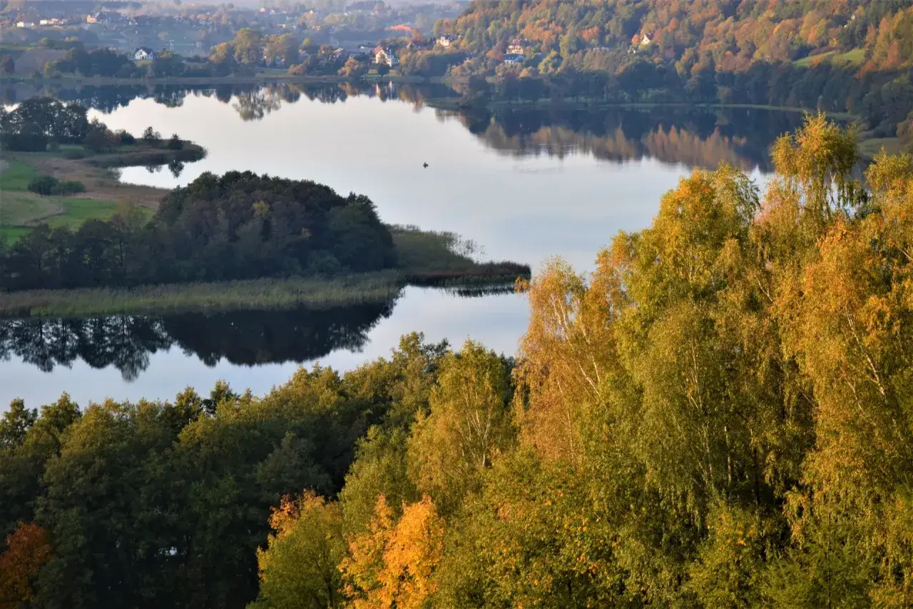 Złota jesień na Kaszubach. Jezioro odbija kolorowe drzewa, a na wodzie widać samotną łódkę.