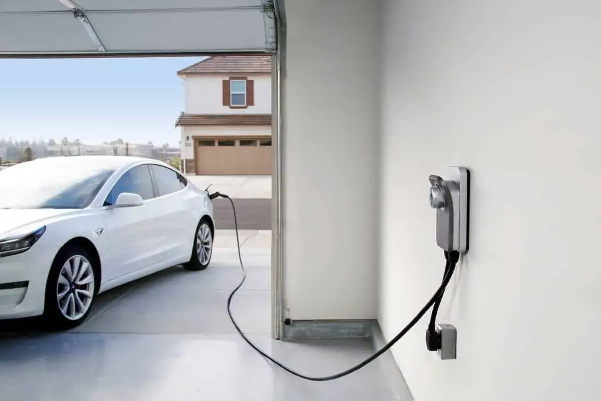 Biała Tesla podłączona do ładowarki w garażu. Zastanawiasz się, jak długo ładuje się Tesla? Czas zależy od wielu czynników.