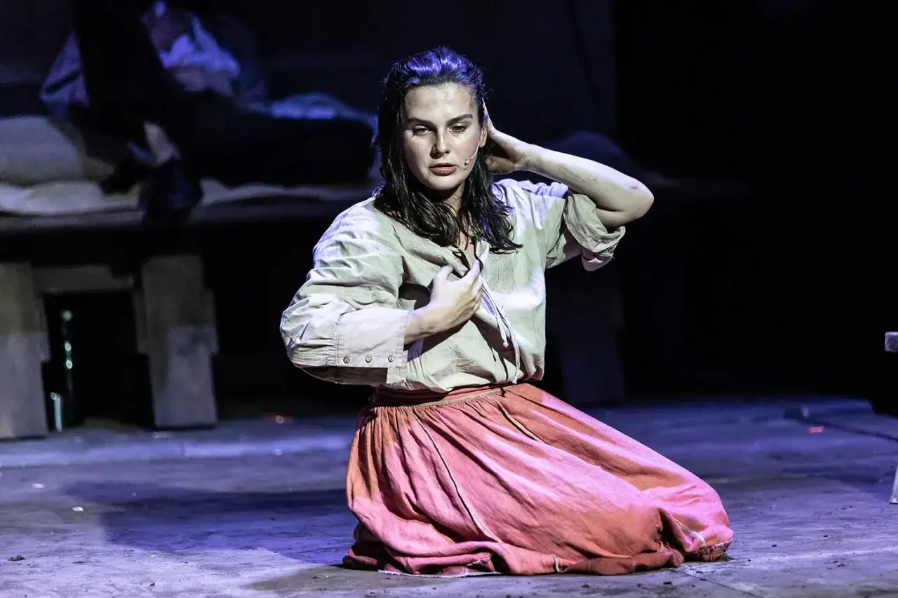 Aktorka na scenie, w stroju z epoki, zastanawia się, ile trwa spektakl w teatrze.