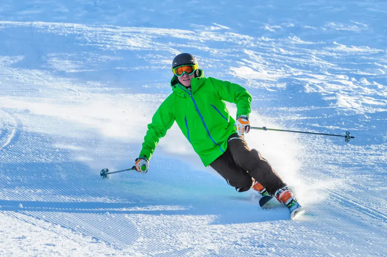 Narciarz w zielonej kurtce wykonuje dynamiczny skręt, tworząc obłok śniegu. To prawdziwa ewolucja na stoku, pełna prędkości i adrenaliny.