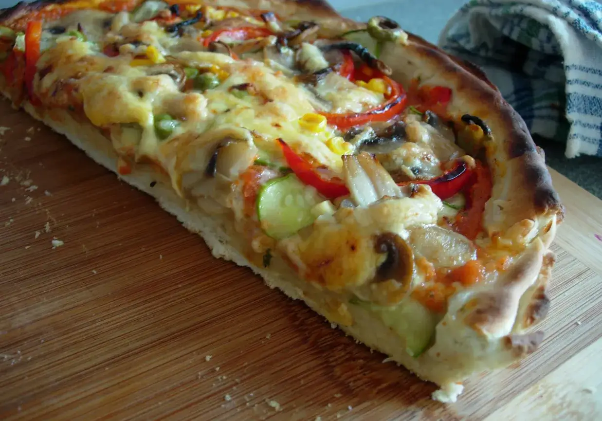 Kawałek pizzy z warzywami i serem. Czy pizza jest lekkostrawna? Ta wygląda apetycznie, ale ciężko ocenić po wyglądzie.