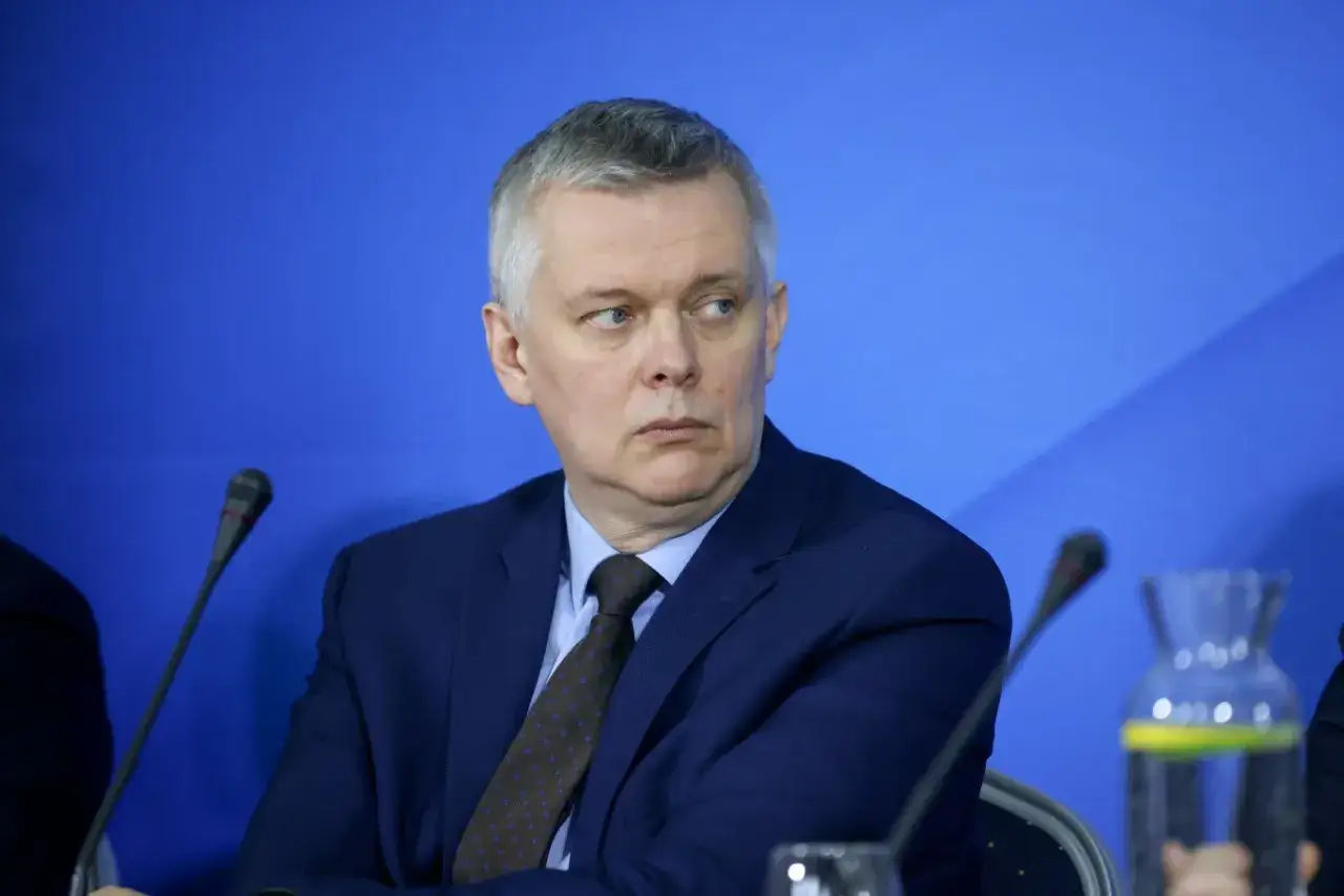 Tomasz Siemoniak, polityk o polskim pochodzeniu, w granatowym garniturze i krawacie, siedzi przy stole konferencyjnym.