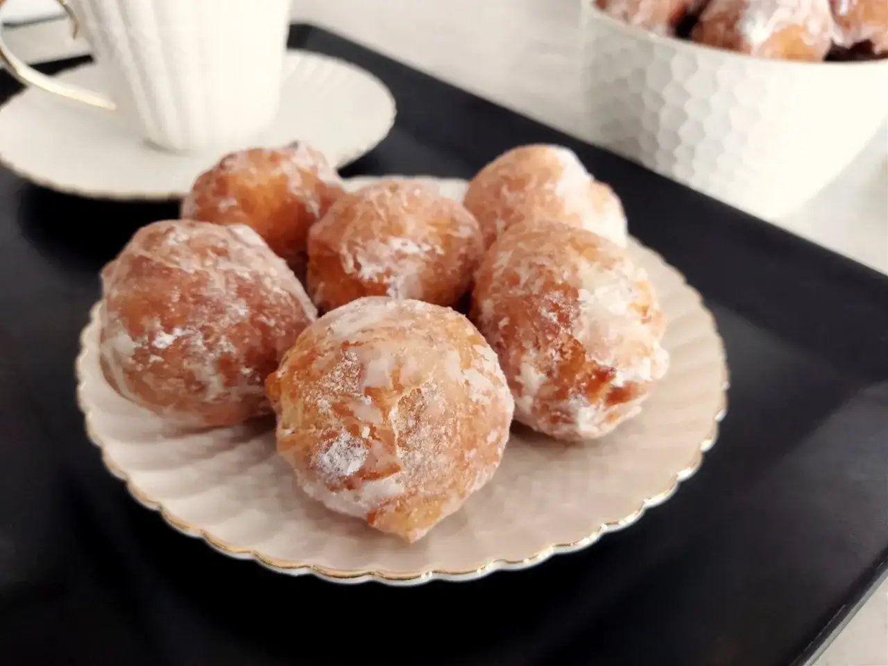 Pyszne pączki z serków homo, oprószone cukrem pudrem, kuszą na talerzyku. Idealne na deser!