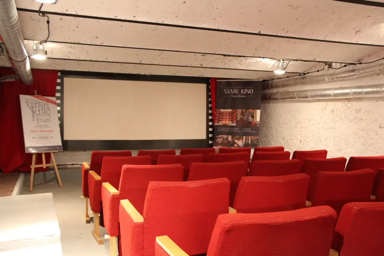 Czerwone fotele kinowe i ekran, obok plansza 
