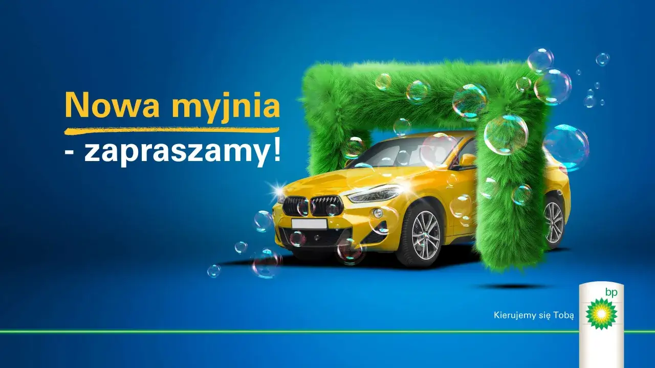 Nowa myjnia BP zaprasza! Żółty samochód w zielonej, puszystej myjni, otoczony bańkami mydlanymi.