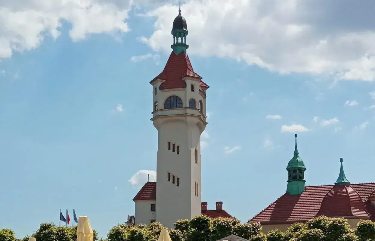 Charakterystyczna latarnia morska Sopot z czerwonym dachem i białymi ścianami, na tle błękitnego nieba z chmurami.