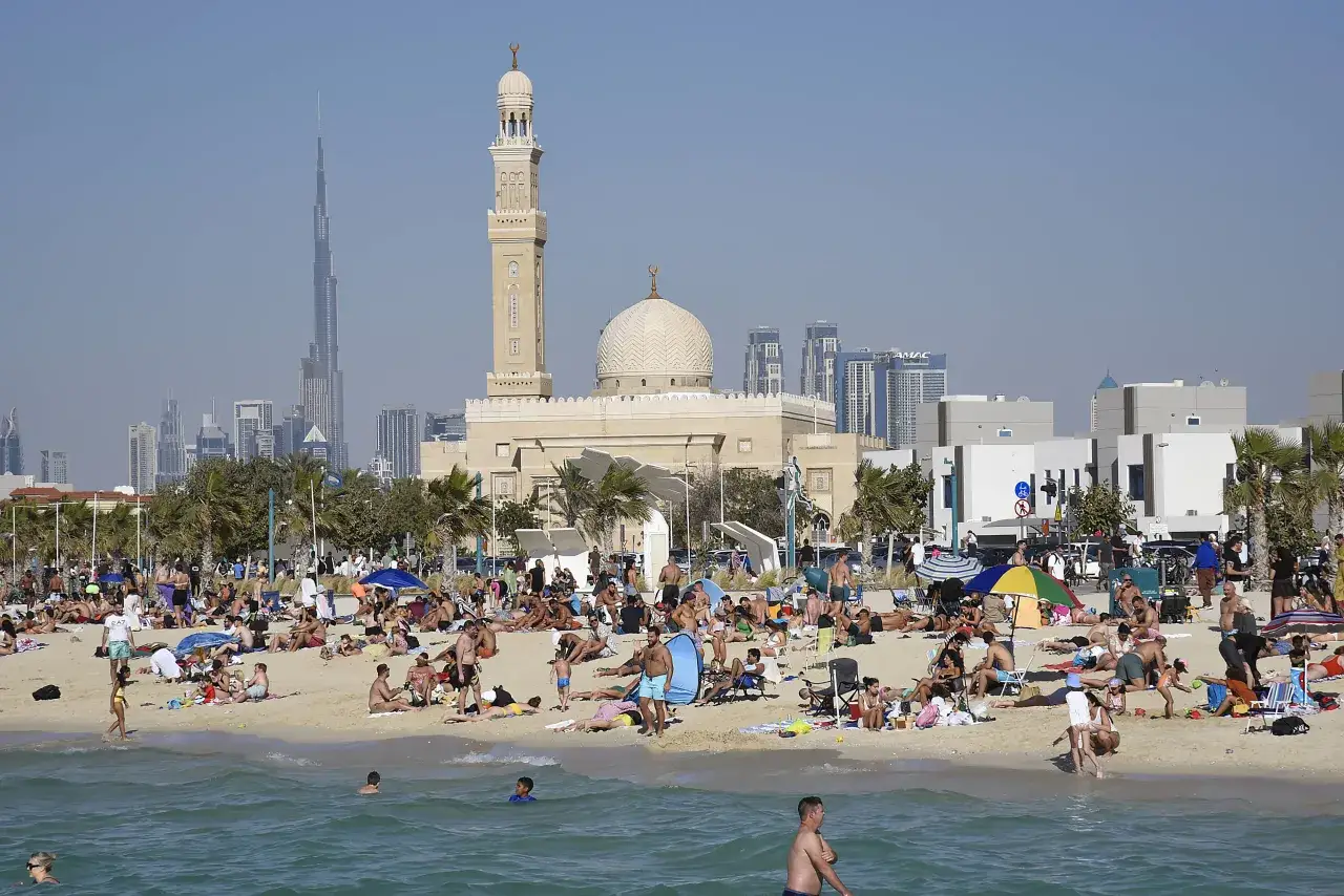 Plaża w Dubaju pełna ludzi, w tle meczet i drapacze chmur. Idealny czas na zwiedzanie to zima, kiedy najlepiej lecieć do Dubaju.