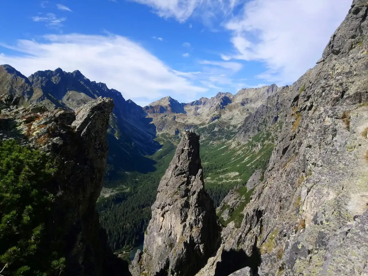 Widok z przełęczy pod Osterwą na skaliste szczyty i zieloną dolinę. Na skalnym ostrym szczycie widać dwie postacie.