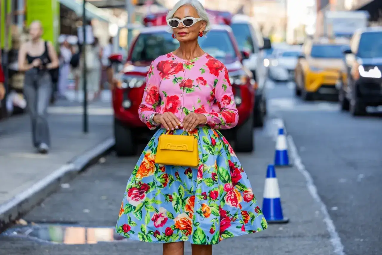 Elegancka kobieta w kwiecistej sukience i różowym kardiganie, z żółtą torebką. Idealna moda na lato, pełna kolorów i radości.