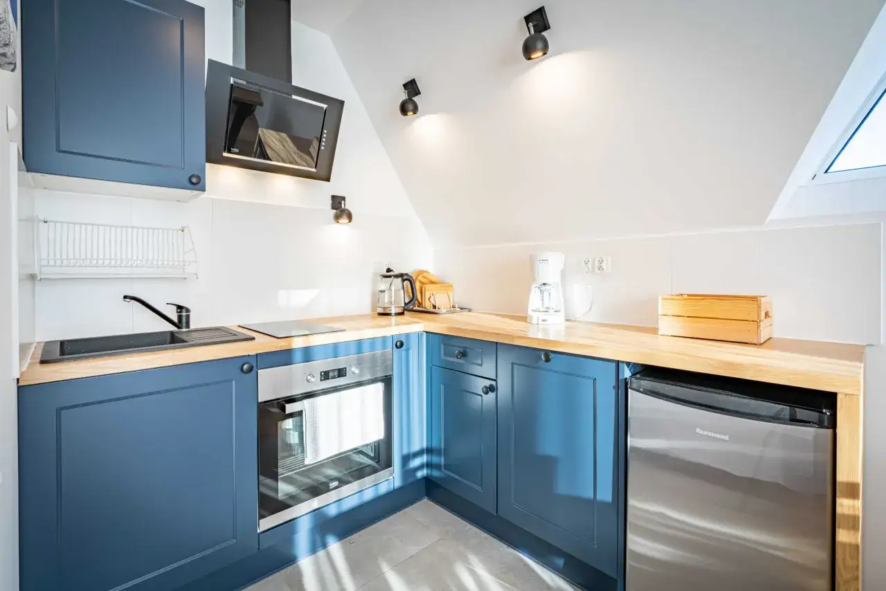 Nowoczesna kuchnia w apartamencie pod wierchem. Granatowe szafki, drewniany blat, piekarnik, czajnik i ekspres do kawy.