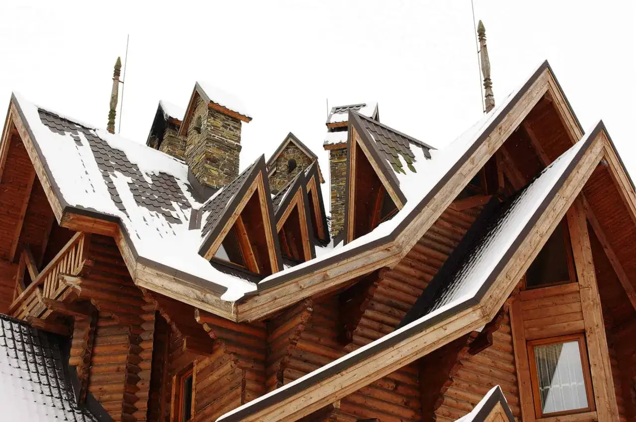 Drewniany dom z wieloma dachami i kominami, pokryty śniegiem. To właśnie lukarna co to za element architektoniczny?