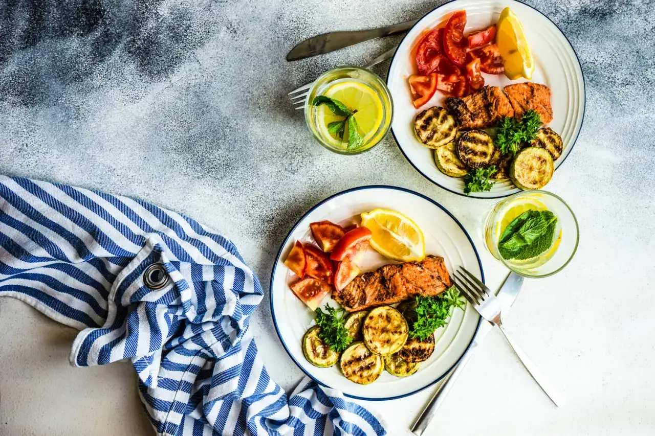 Dwa talerze z łososiem, grillowaną cukinią i pomidorami. Woda z cytryną i miętą. Idealne danie na dieta niskowęglowodanowa efekty.