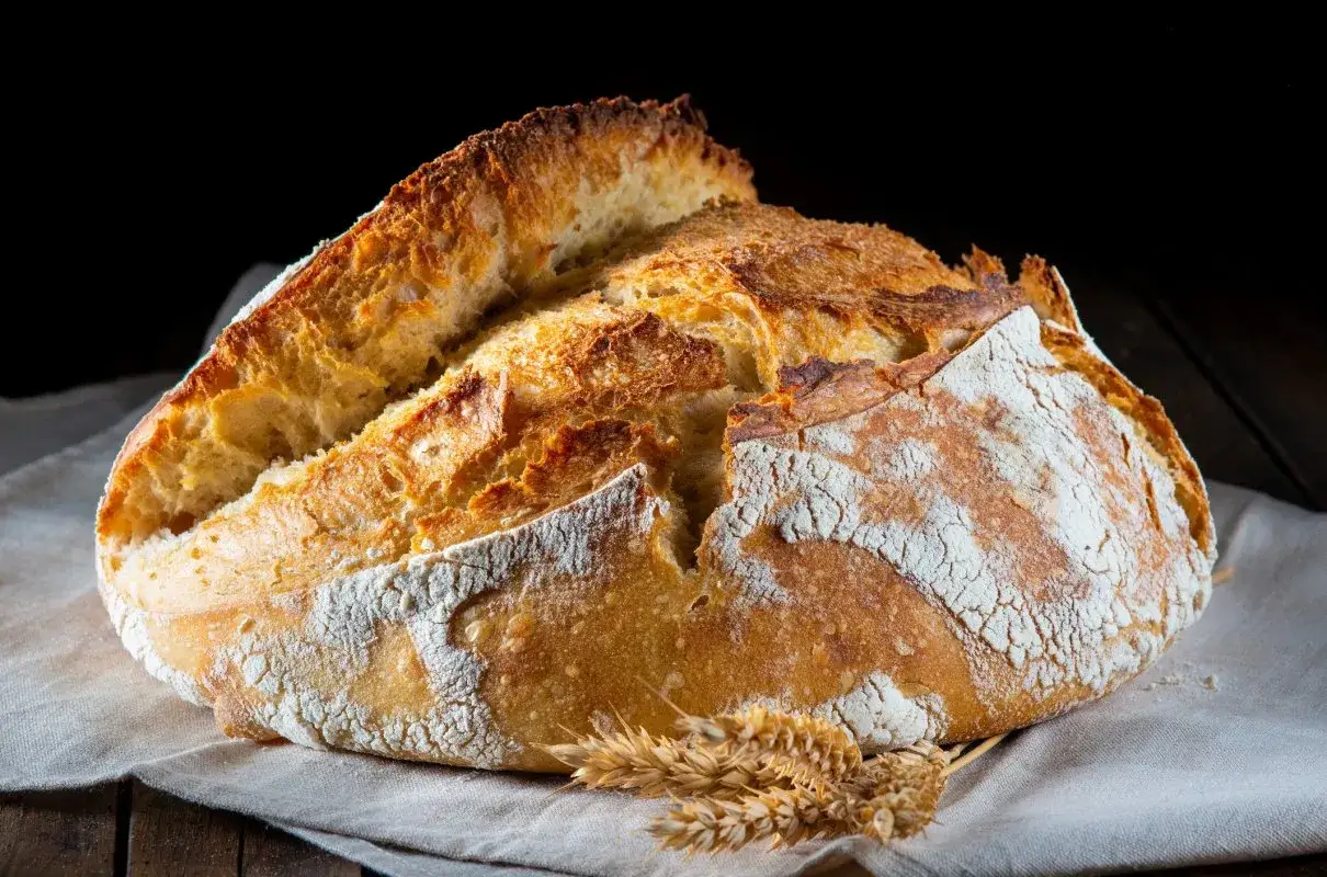 Chrupiący bochenek chleba na lnianej serwetce, z kłosami zbóż. Idealny na pytanie: ile chleba na 20 osób?