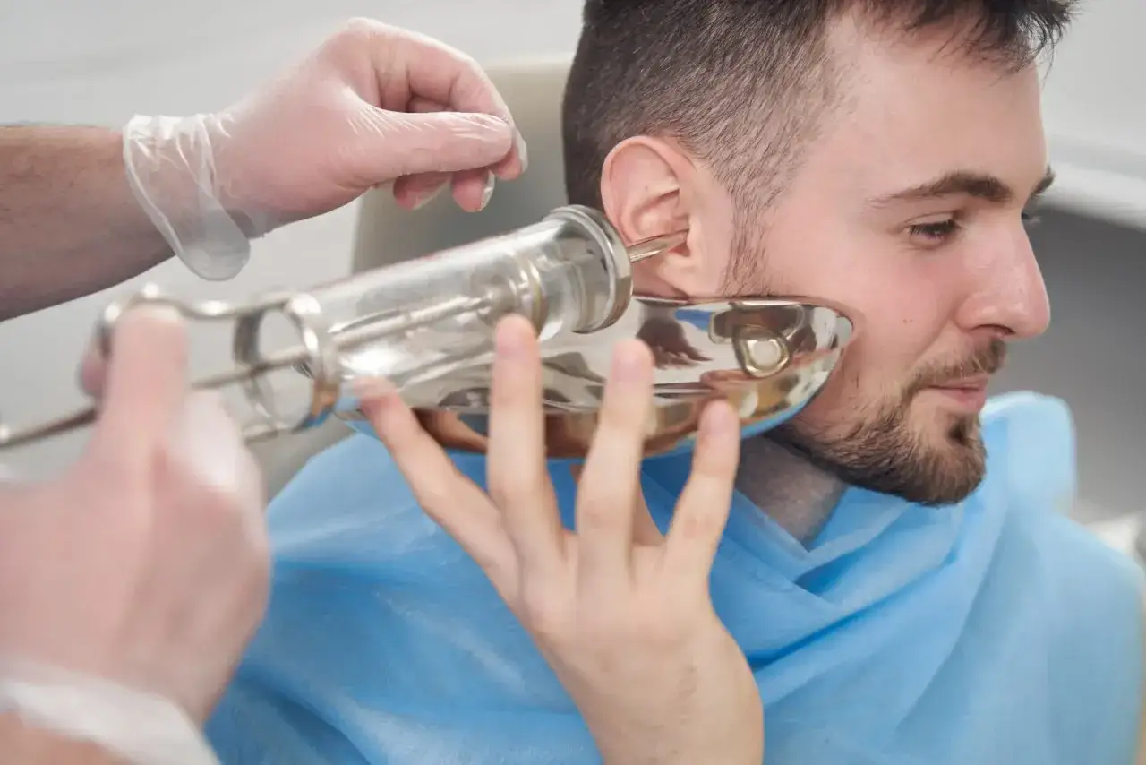 Laryngolog w rękawiczkach wykonuje czyszczenie uszu pacjentowi za pomocą specjalistycznego narzędzia.