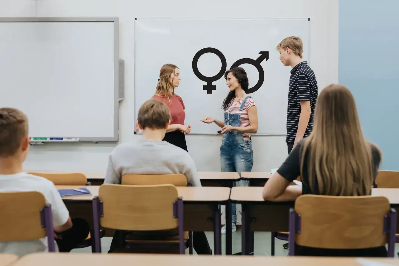 Uczniowie dyskutują o symbolach płci na tablicy. To przykład, jak można omawiać cele edukacyjne.