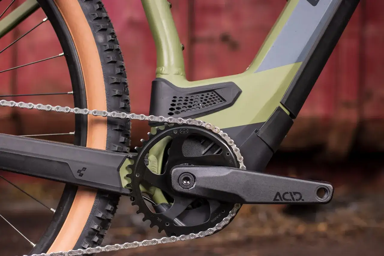 Zbliżenie na rower elektryczny: widoczna zębatka, korba ACID i łańcuch o standardowej szerokości.