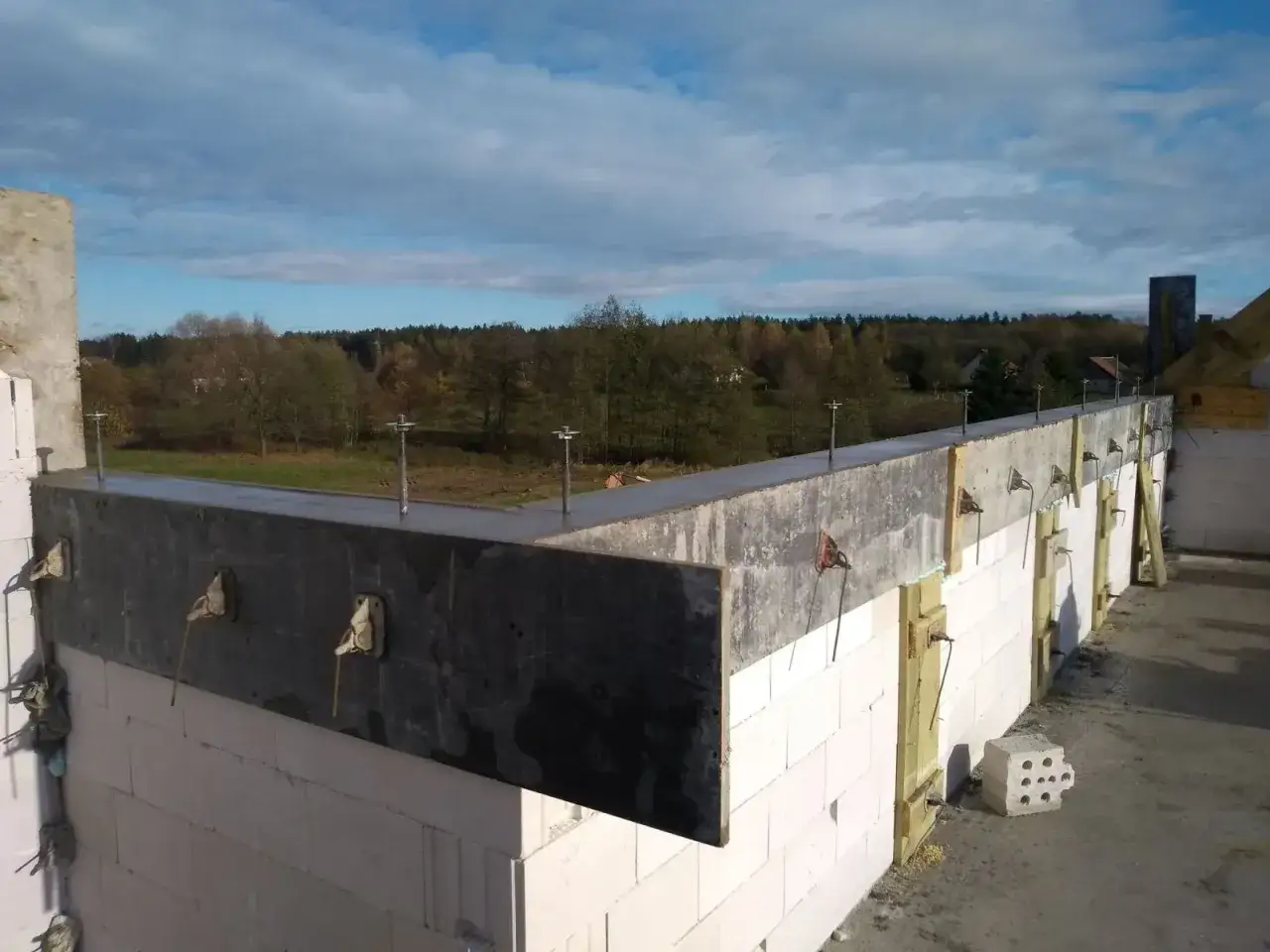Szpilki do murłaty w betonie, gotowe do montażu więźby dachowej. W tle jesienny krajobraz.