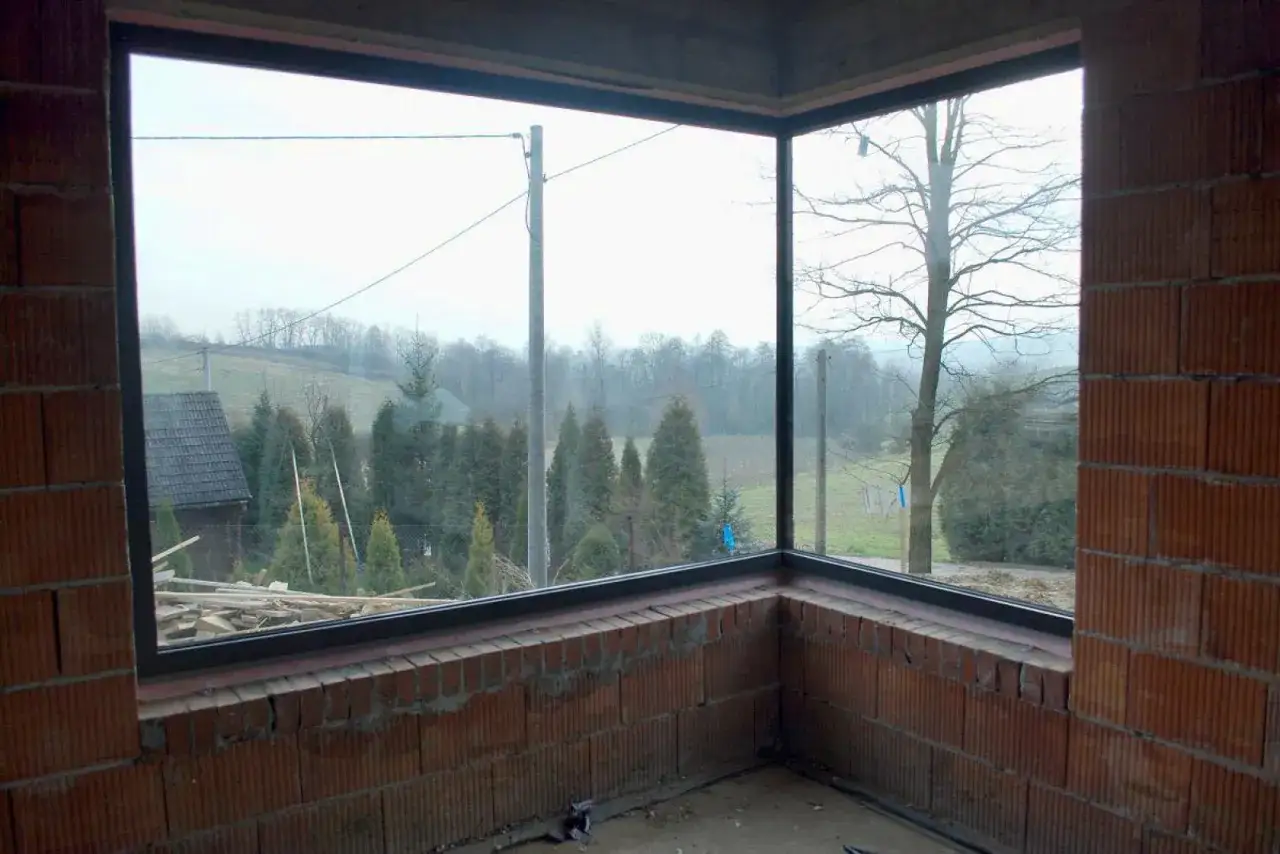 Widok z narożnego okna na wiejski krajobraz. Widać różne sposoby otwierania okien, które zapewniają dostęp do świeżego powietrza.