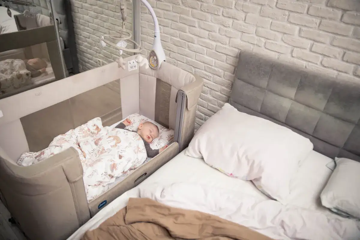 Ł&oacute;żeczko dostawne z niemowlakiem obok ł&oacute;żka rodzic&oacute;w