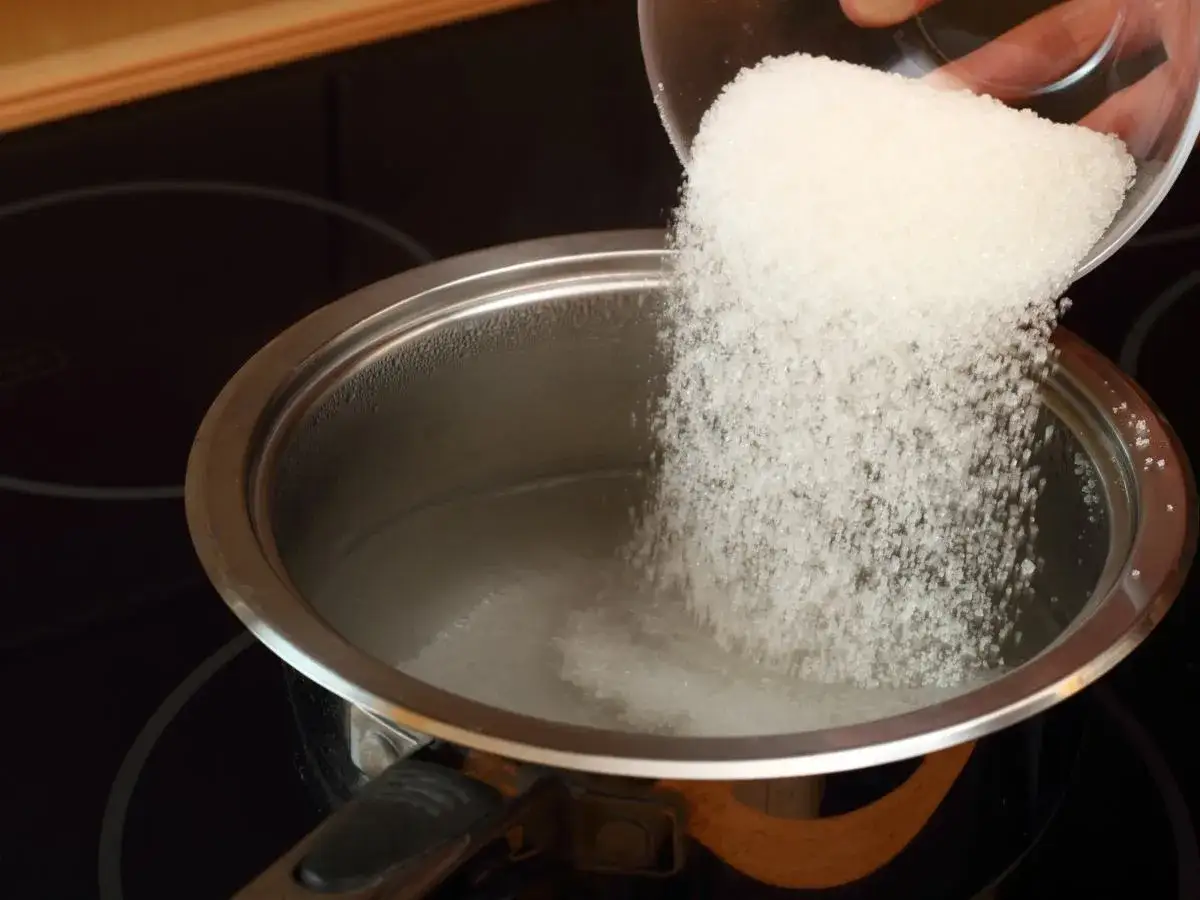 Wsypywanie cukru do garnka z wodą to pierwszy krok, jak przygotować domowy syrop cukrowy (simple syrup).