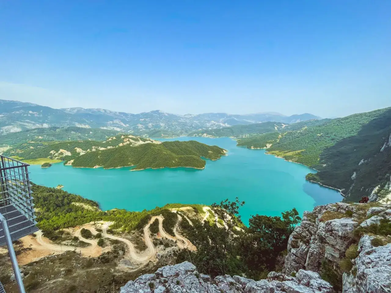 Widok na turkusowe wody Bovilla Lake otoczone zielonymi wzgórzami i górami. Kręta droga prowadzi do punktu widokowego.