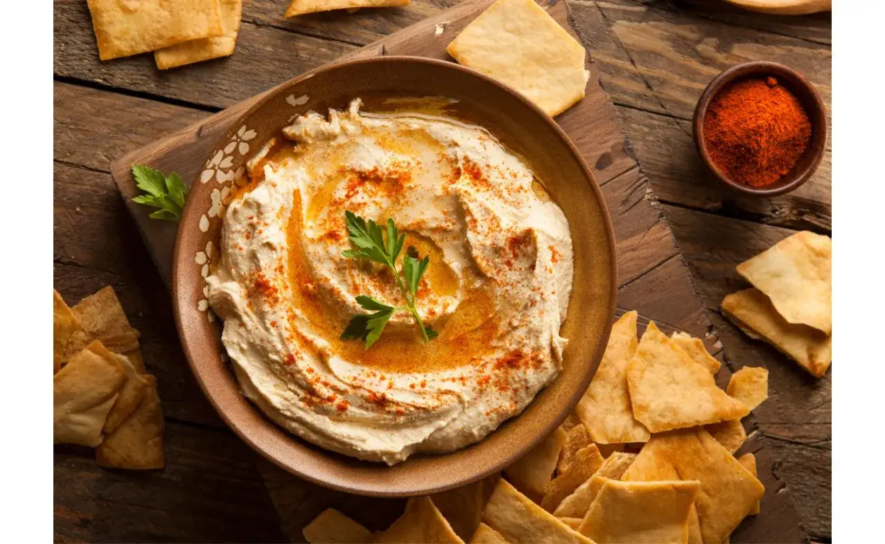 Kremowy hummus z ciecierzycy, polany oliwą i posypany papryką, podany z chrupiącymi kawałkami pity.