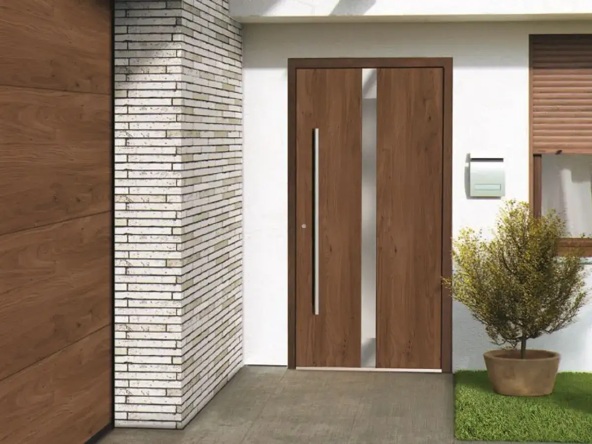 Nowe, nowoczesne, brązowe drzwi wejściowe z pionowym przeszkleniem, obok ceglanej kolumny i donicy z krzewem.