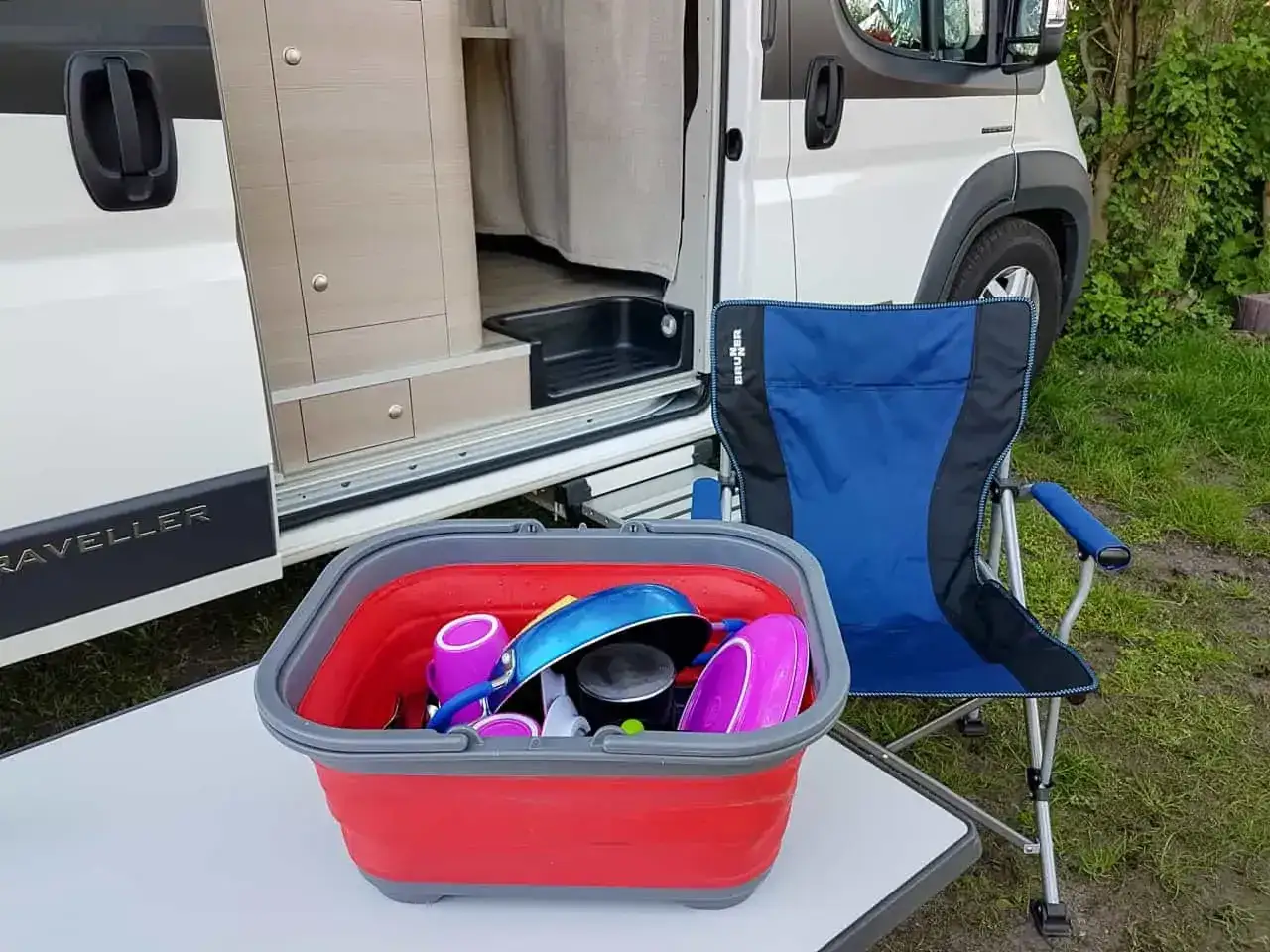 Składana miska z naczyniami i krzesło turystyczne obok kampera. Praktyczne gadżety do kampera ułatwiające życie na kempingu.