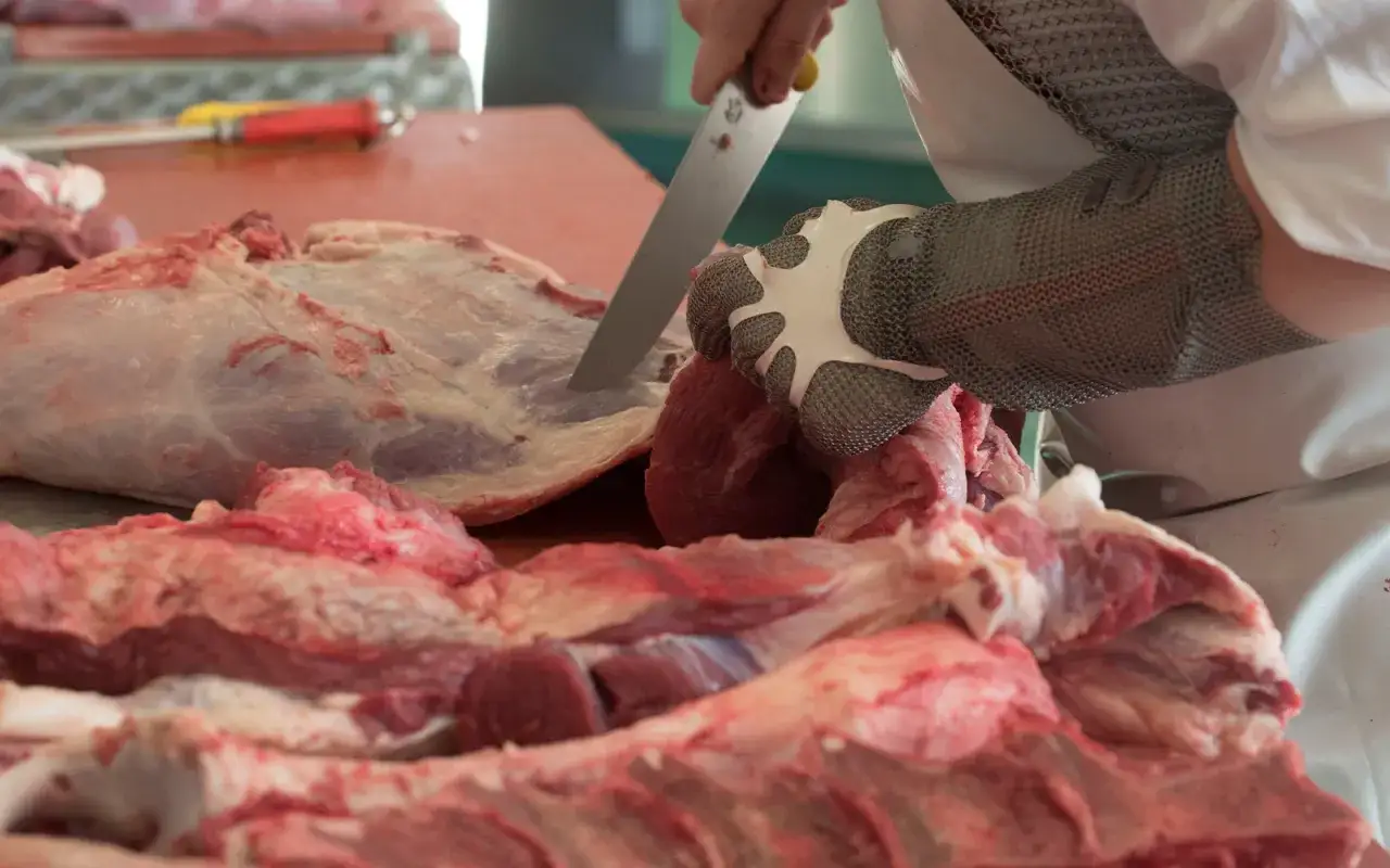 Rzeźnik w rękawicy z siatki metalowej używa noża, by pozbyć się błon i ścięgien z mięsa. Proste triki ułatwiają pracę.