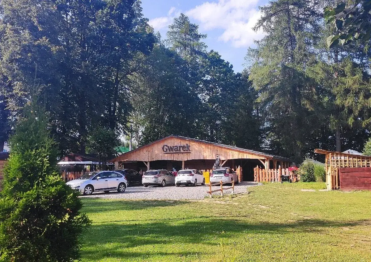 Drewniana restauracja Gwarek w Polańczyku, otoczona zielenią, z zaparkowanymi samochodami.