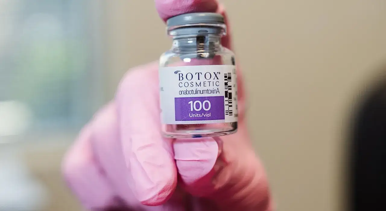 R&oacute;żowa rękawiczka trzyma fiolkę z preparatem BOTOX COSMETIC. To właśnie botox co to jest &ndash; substancja stosowana w medycynie estetycznej.